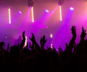 Crowd cheering at concert with pink stage lights.